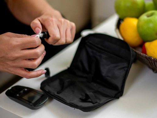 A pair of hands using a diabetes test strip above a blood glucose meter and case. Hamilton Medical Center