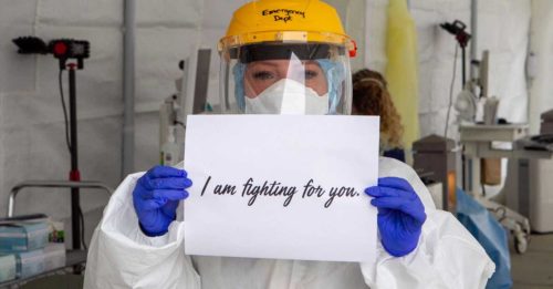 Nurse wearing ppe holding a sign that says "I'm fighting for you"